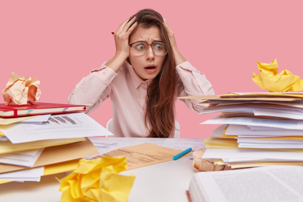 Illustration of a teacher at a desk with a stack of papers, looking overwhelmed, representing the challenges of workload and coping faced by casual relief teachers.